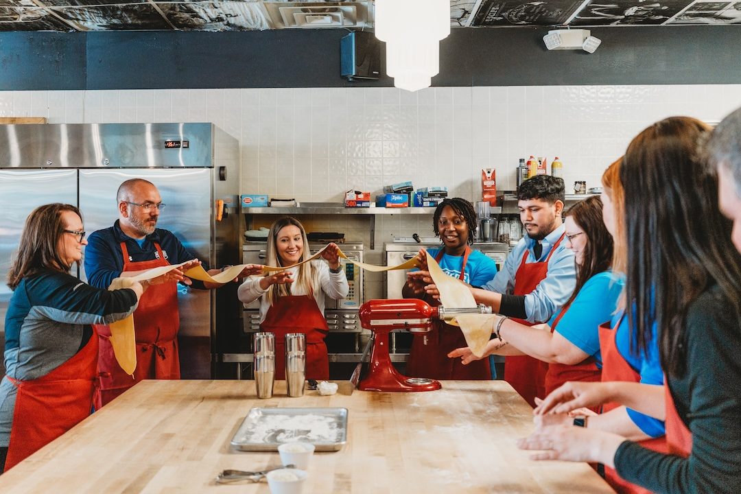 A team stretching fresh pasta together during a hands-on experience at The Local Epicurean in Grand Rapids.